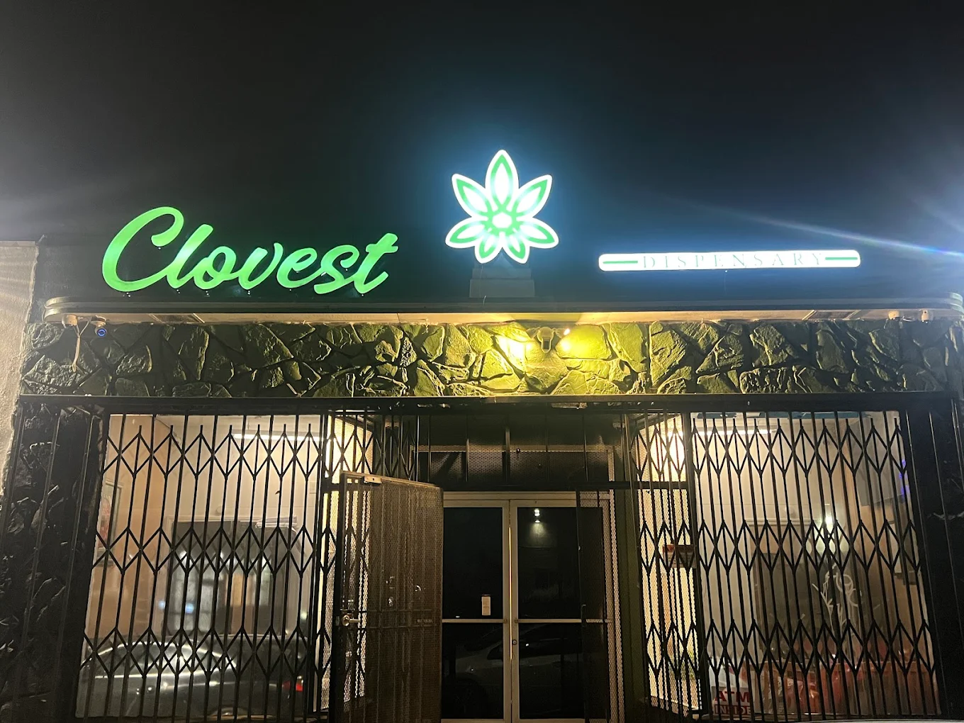 Clovest Retail 6563 storefront with green neon signage and security gates at night